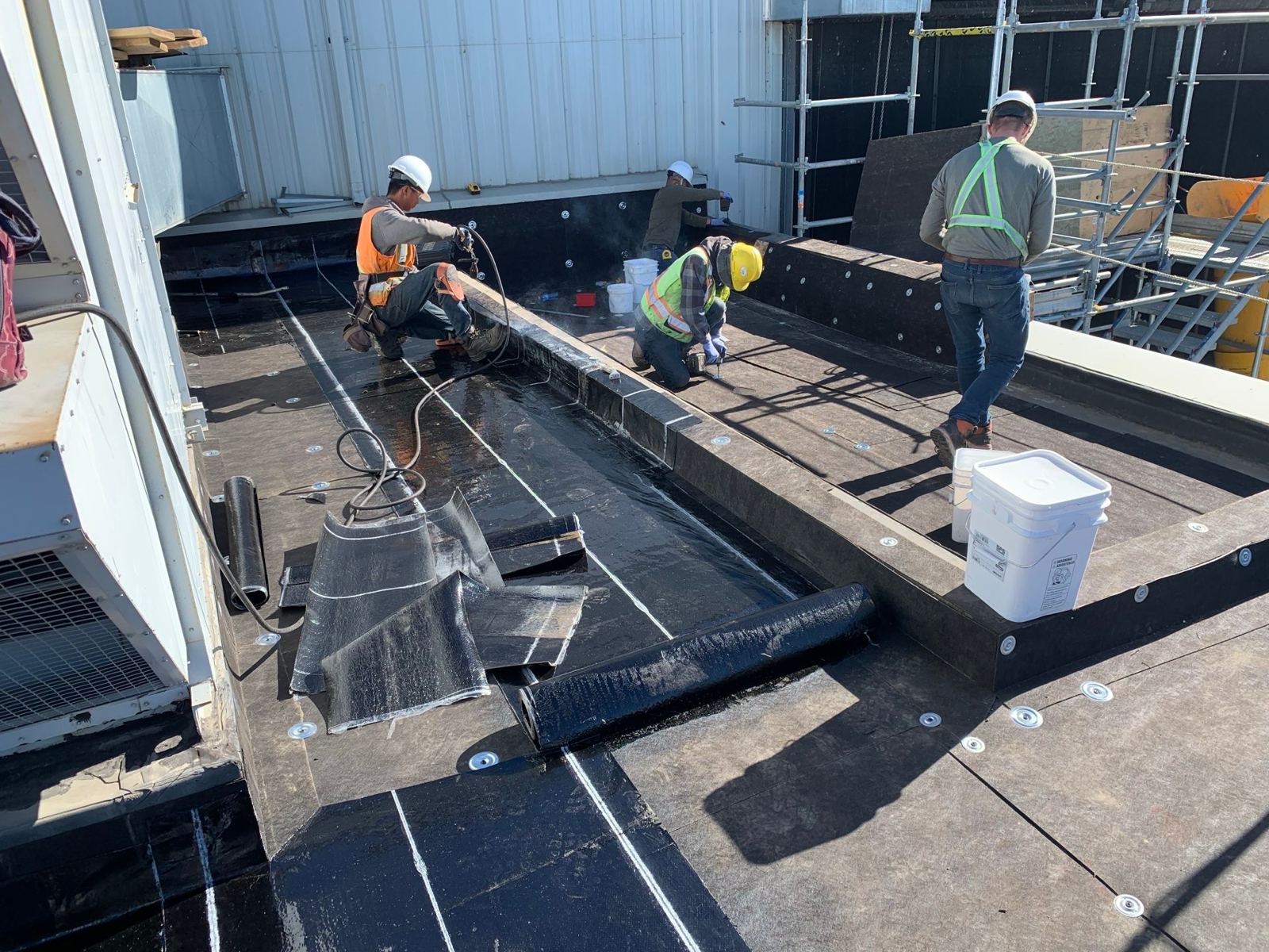 City Roofing crew installing torch-on membrane up a parapet wall