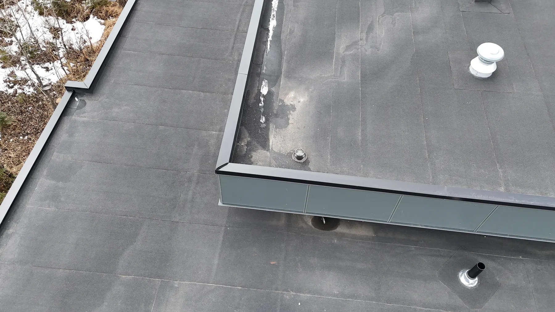 Flat roof membrane meeting a parapet wall, with a roof vent