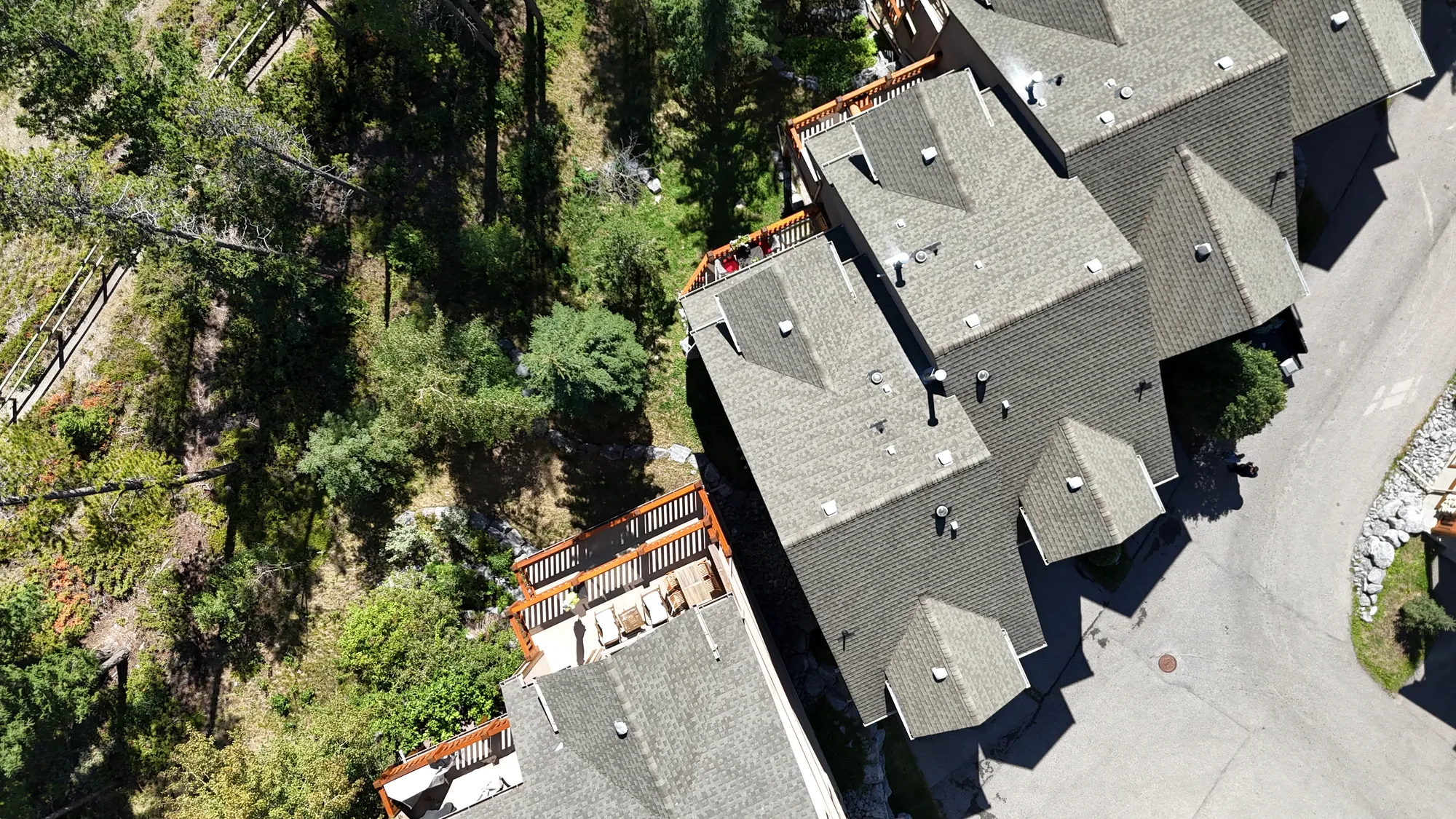 Aerial view of a row of townhouses with grey asphalt shingle roofs beside a wooded slope