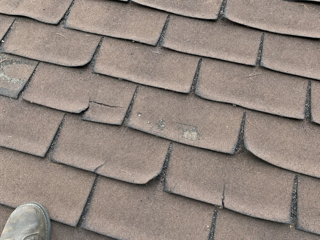 Old brown shingles with curled edges, a crack and bare patches where granules wore off (illustration)